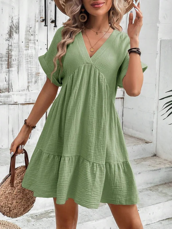 "Green flowy v-neck mini dress with pleated skirt, perfect for a casual day out. Made of lightweight, breathable material."