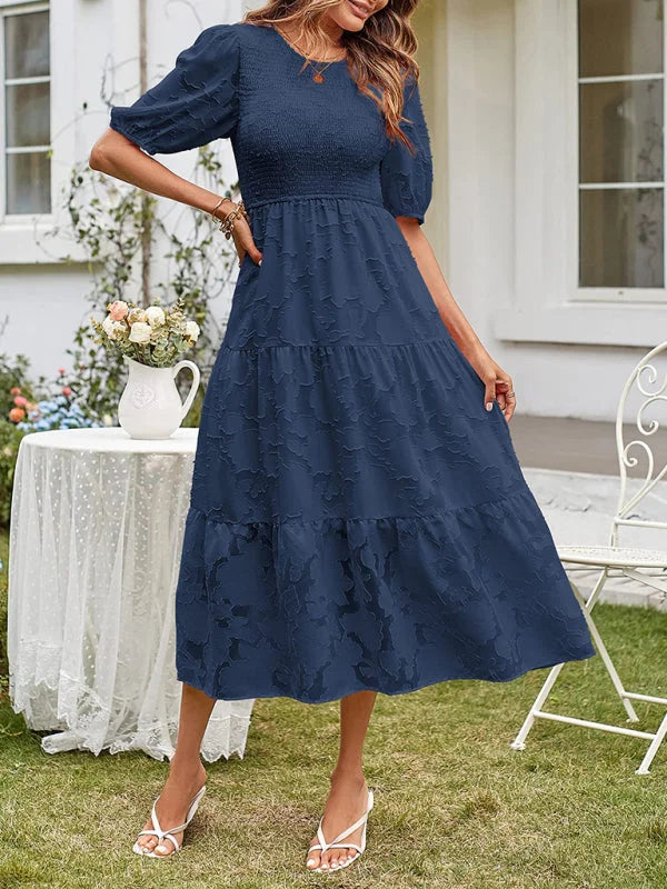 Tiered midi dress in light blue with textured pattern. Features cap sleeves and flowy silhouette, perfect for a casual yet…