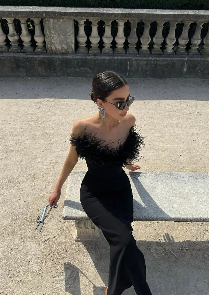 "Sleek black strapless maxi dress with feather details, a rebellious twist on a classic design for bold, fashion-forward…
