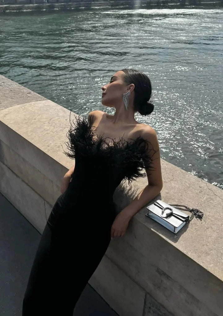 Black strapless maxi dress with feather details. Sleek and stylish design for rebellious women.