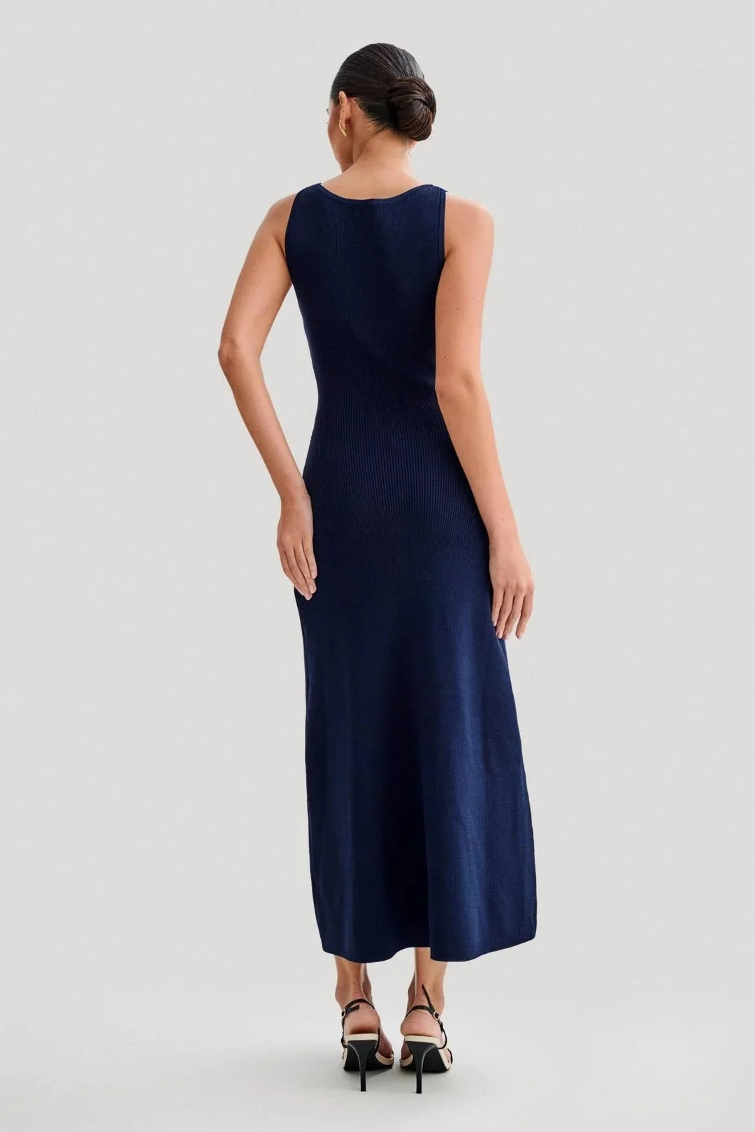 Sleeveless dress in black with front buttons, tailored silhouette on a mannequin.